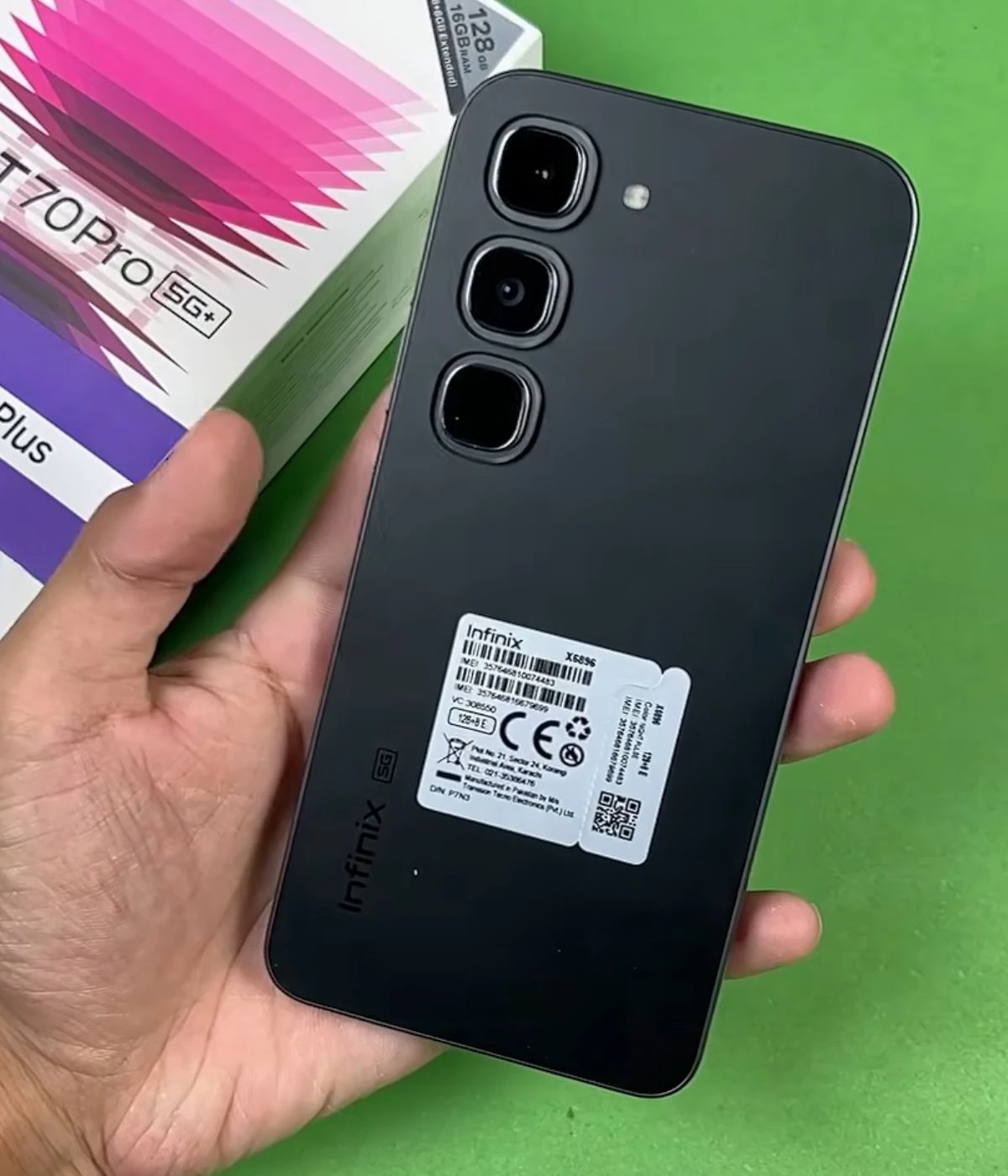 Infinix Hot 70 Pro smartphone held in hand with camera setup and packaging