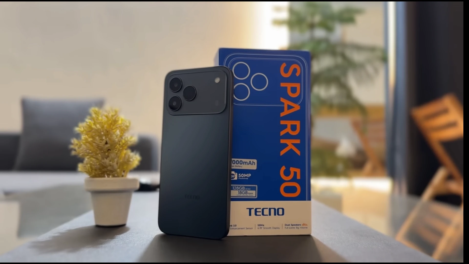 TECNO Spark 50 smartphone with packaging on a table next to a decorative plant
